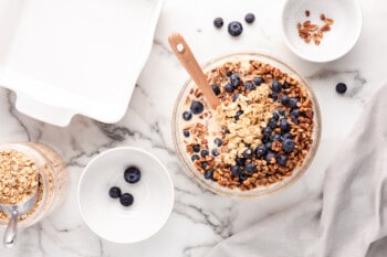 adding nuts and blueberries to oatmeal mixture in a glass bowl