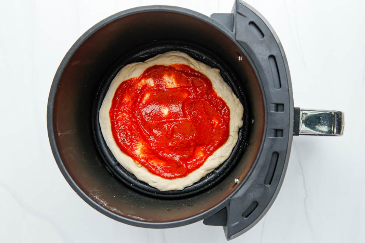 sauce on pizza dough in air fryer before cooking