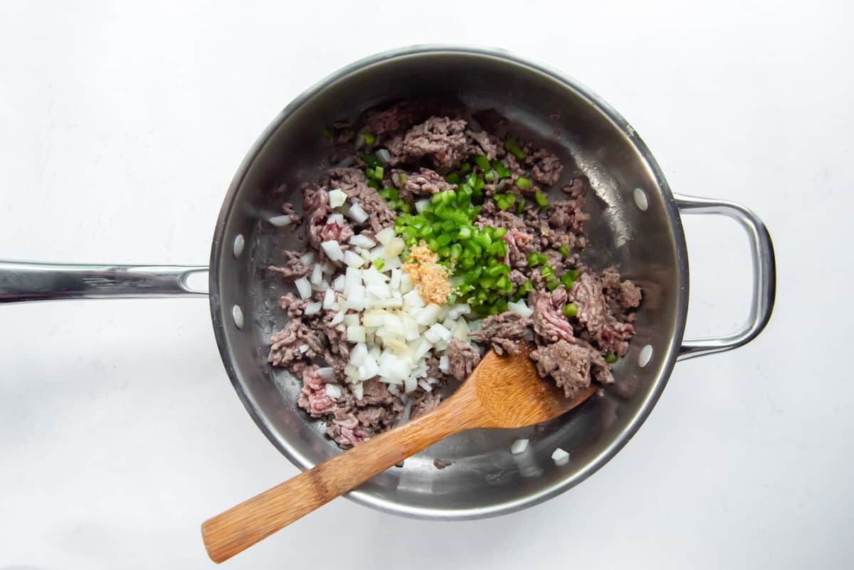 ground beef, chopped onion, diced jalapeños, and garlic in a pan with a wood spoon