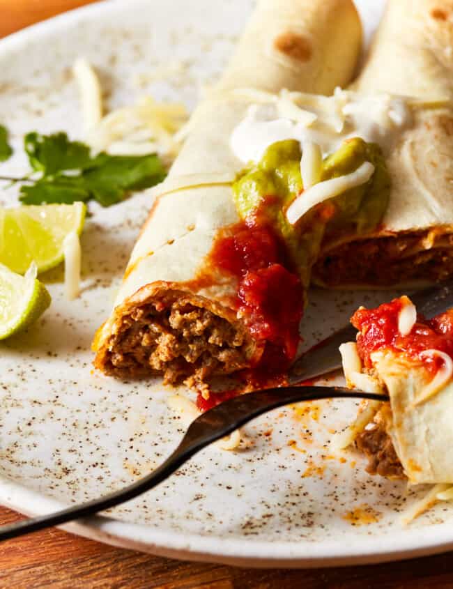 beef taquitos on a white plate with a fork.