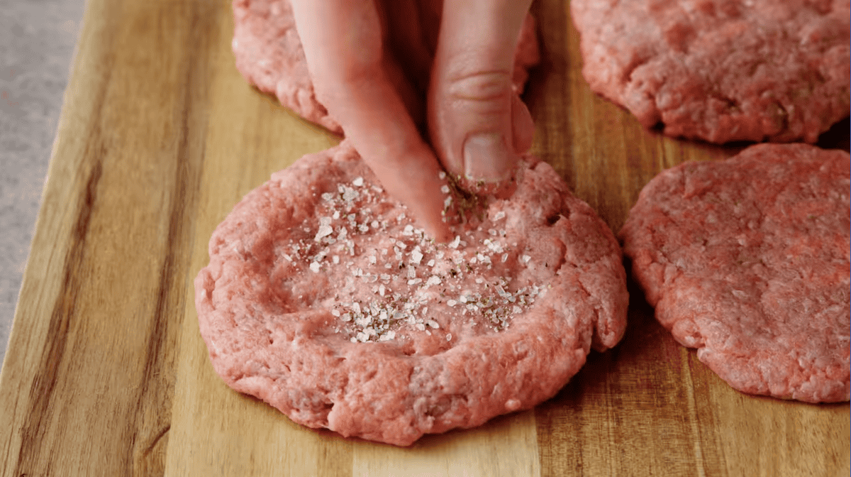 seasoning raw burger patties with salt and pepper.