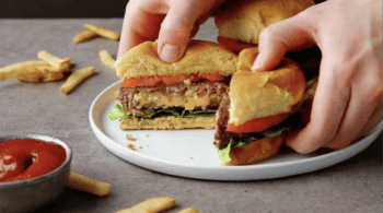 pulling apart a juicy lucy burger to show the molten cheese middle.