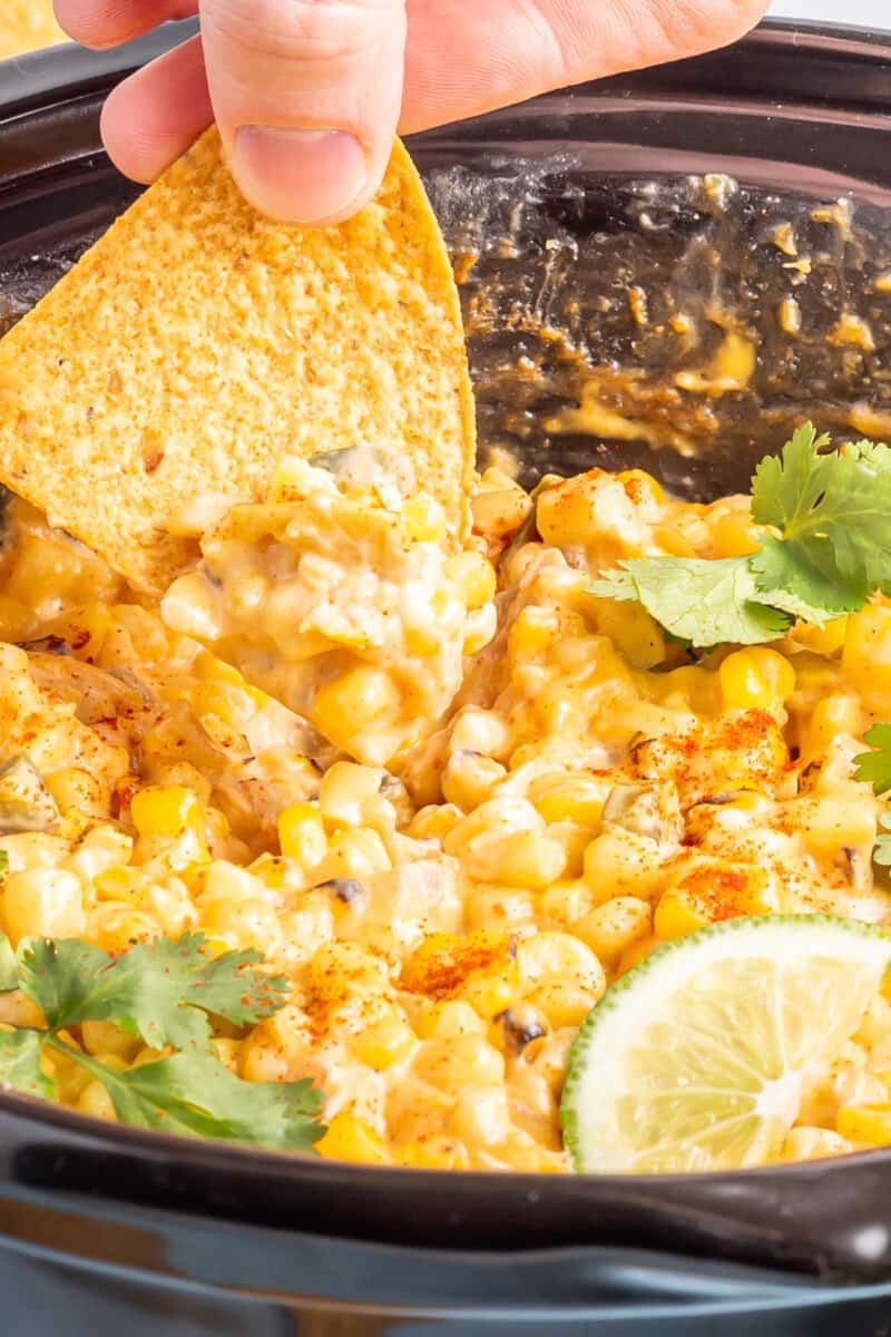 a hand dipping a chip into crockpot corn dip in a crockpot.