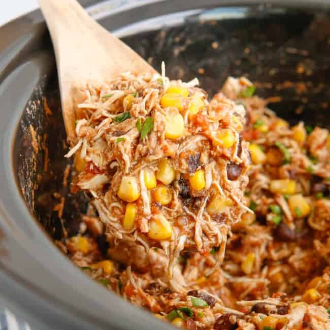 close up of crockpot mexican shredded chicken in a crockpot with a wooden spoon.