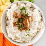 overhead image of french onion dip in a white bowl on a serving platter surrounded by chips, celery sticks, and carrot sticks