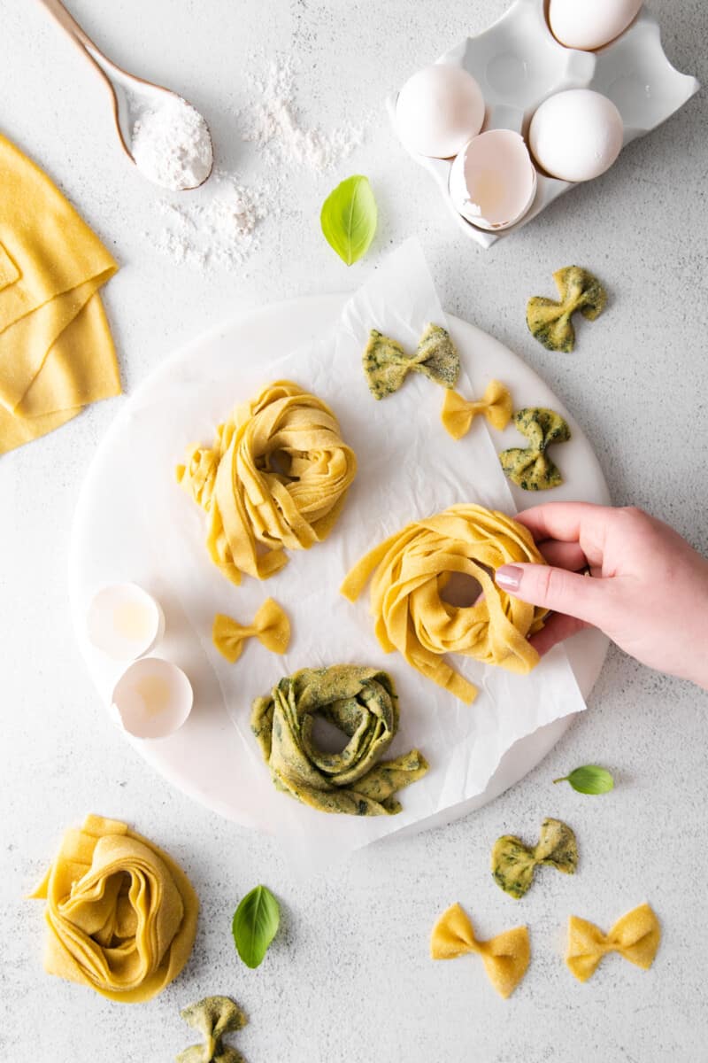 hand grabbing 1 of 3 nests of homemade pasta on a round marble server.