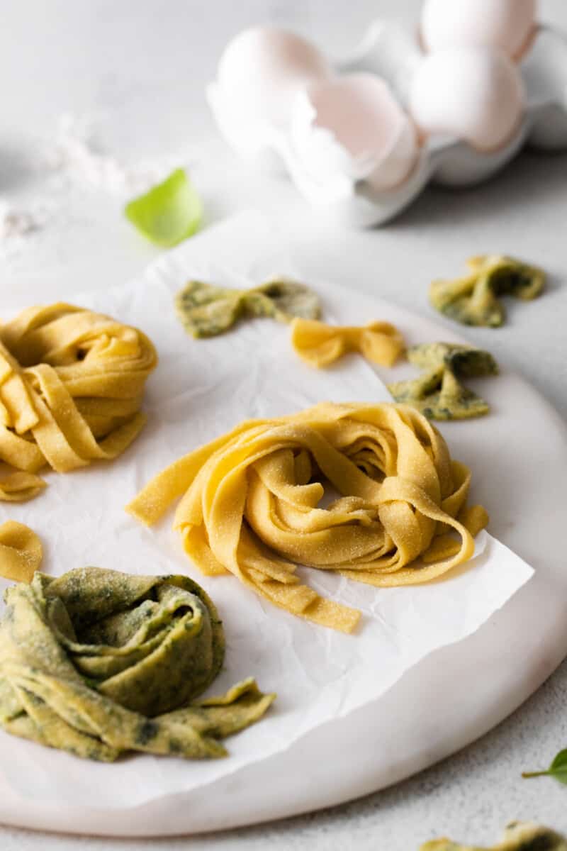 close up of 3 nests of homemade pasta on a round marble server in front of a carton of eggs.