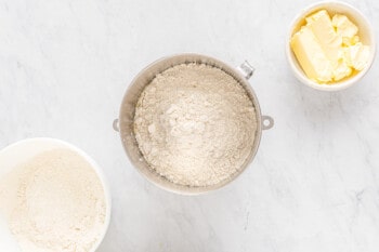 A bakery-style cinnamon roll made with a bowl of flour, butter, and sugar on a marble countertop.