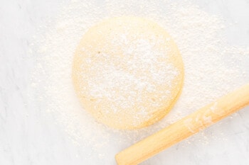 A bakery style cinnamon roll covered in powdered sugar, pictured next to a wooden spoon.