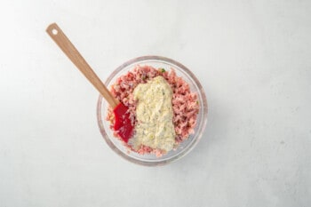 ham salad and mayonnaise sauce in a glass bowl with a rubber spatula.