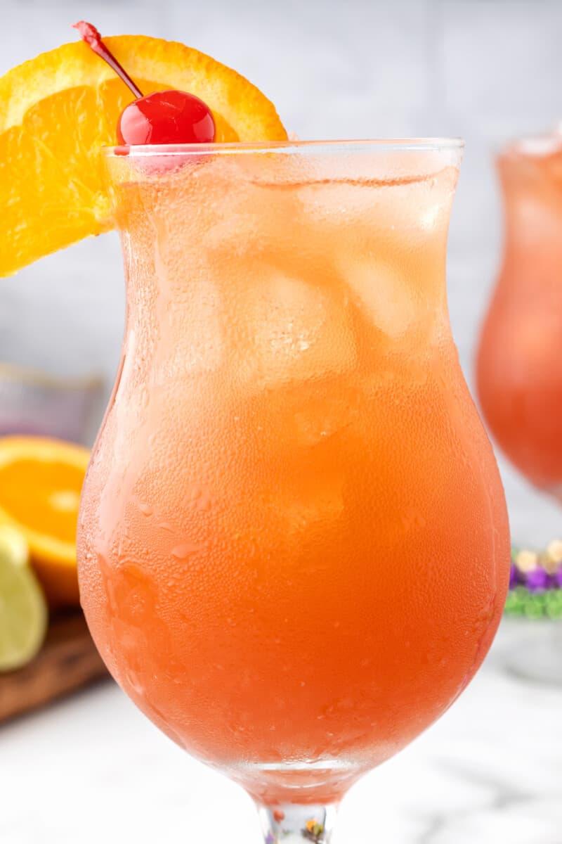 hurricane cocktail in a glass garnished with an orange slice and a cherry