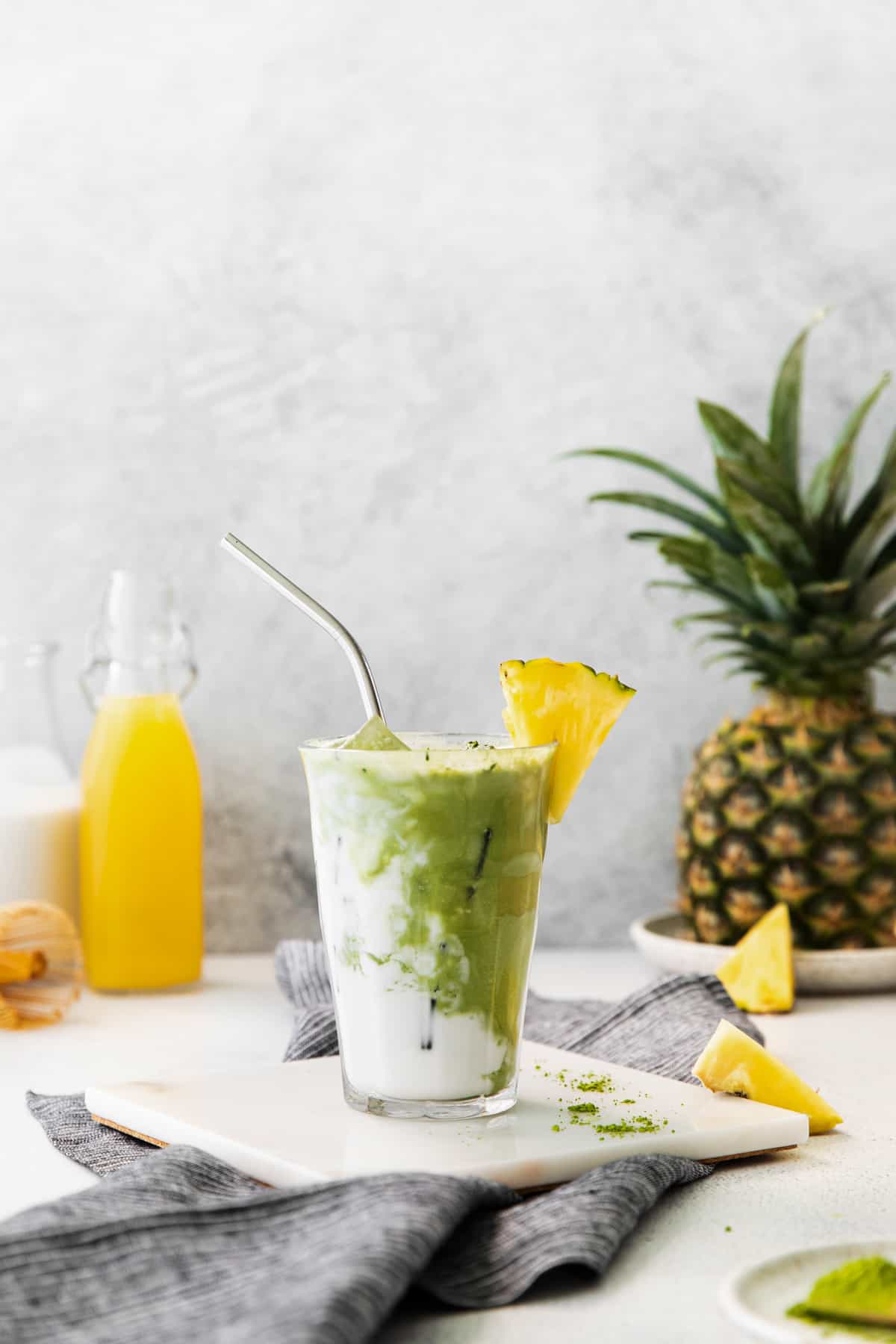 pineapple matcha drink on a white trivet with a stainless steel straw..