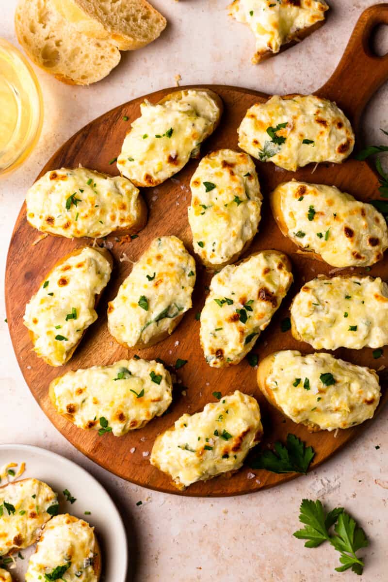 bruschetta topped with artichoke dip on a wooden platter