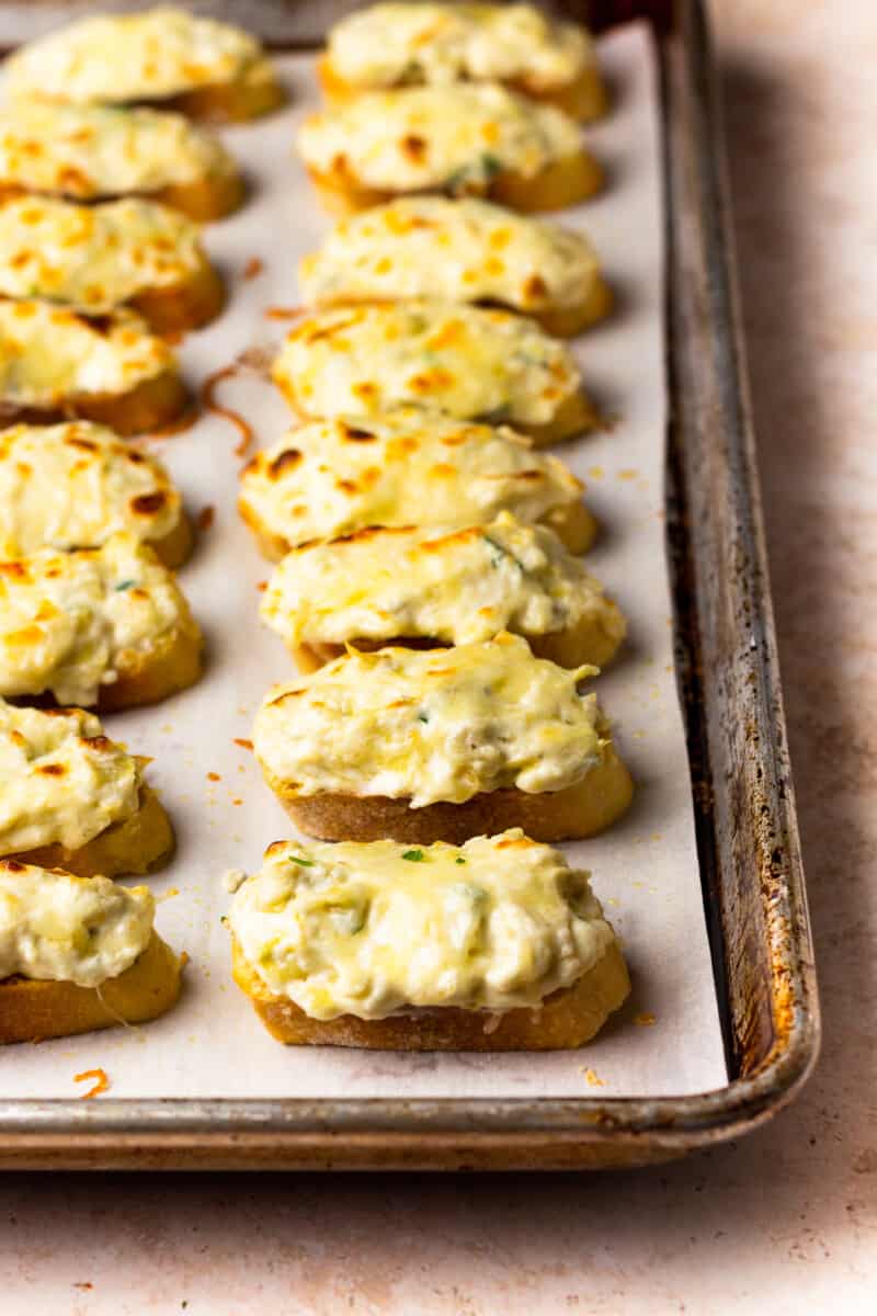 artichoke dip bruschetta lined up on a baking tray