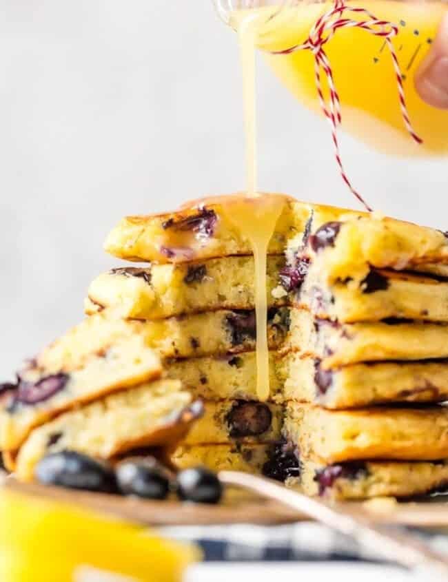 A stack of blueberry pancakes being drizzled with lemon juice and chocolate sauce.