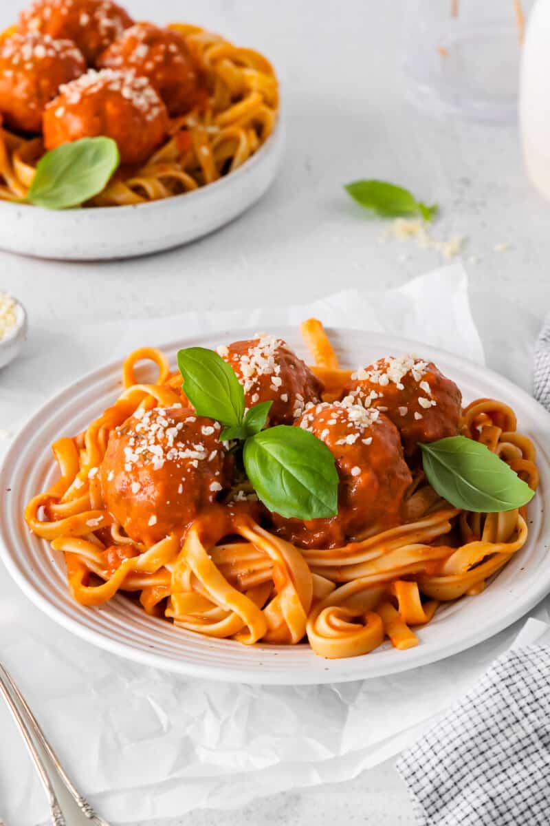 chicken parmesan meatballs over spaghetti in a white bowl.