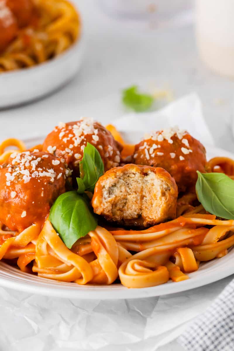 a bitten chicken parmesan meatball over spaghetti in a white bowl.