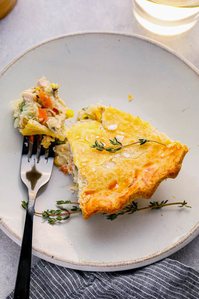 a forkful of chicken pot pie next to a slice of chicken pot pie on a white plate.