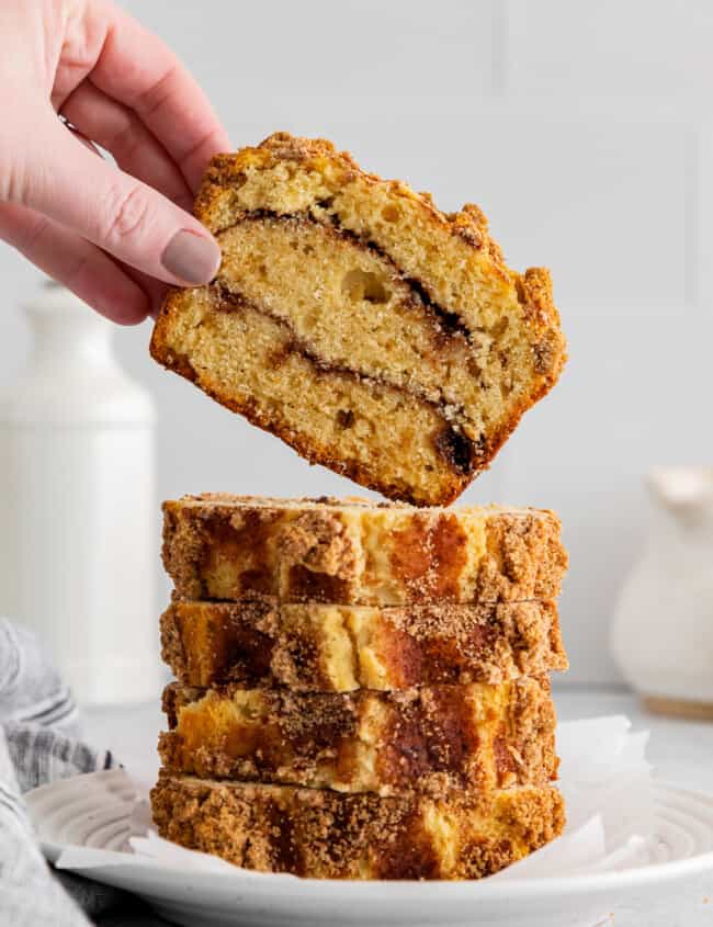 hand grabbing 1 of 5 slices of cinnamon roll bread stacked on a white plate.