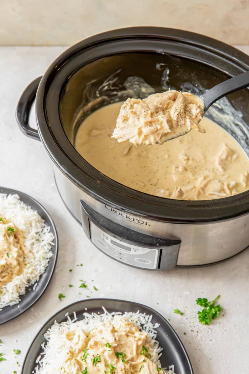 lifting a spoonful of creamy shredded chicken from a crockpot.