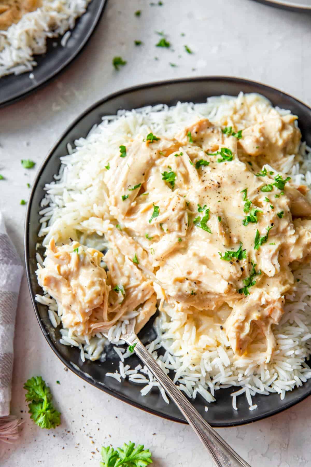 shredded chicken smothered in gravy over rice in a black bowl.