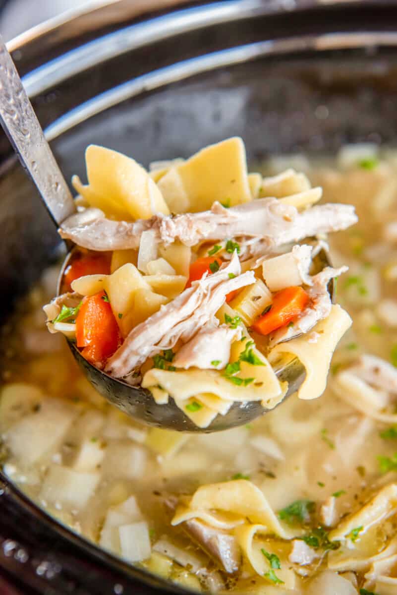 a ladleful of crockpot chicken noodle soup in a crockpot.