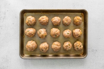 15 rolled unbaked chicken parmesan meatballs on a sheet tray.