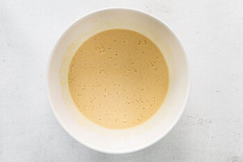 overhead view of mixed wet ingredients for cinnamon roll bread in a white bowl.