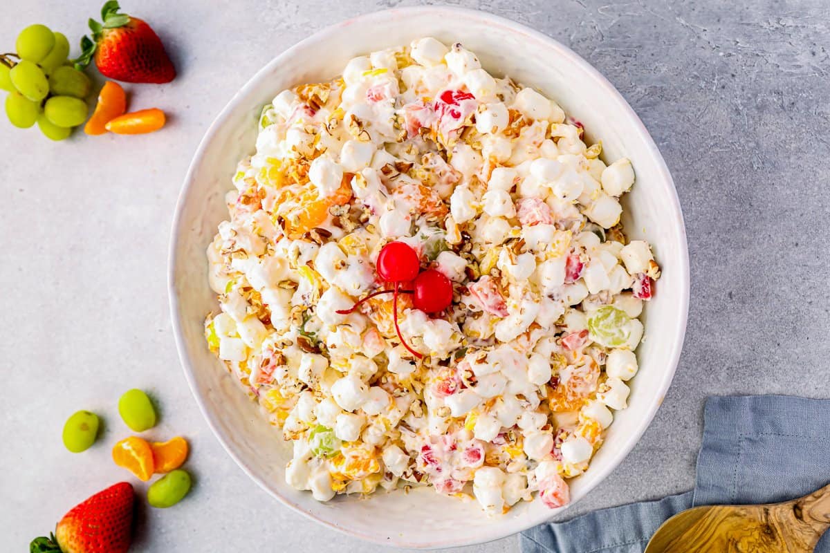 marshmallow salad in a glass bowl with pecans and maraschino cherries.