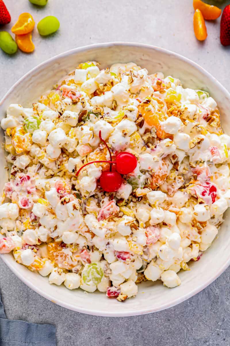 marshmallow salad in a white serving bowl with 2 maraschino cherries.