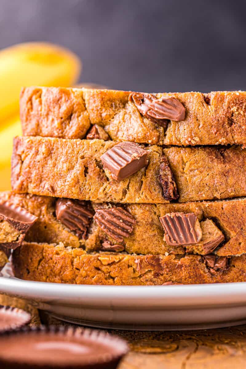 close up of 4 reeses peanut butter cup banana bread slices stacked on a white plate.