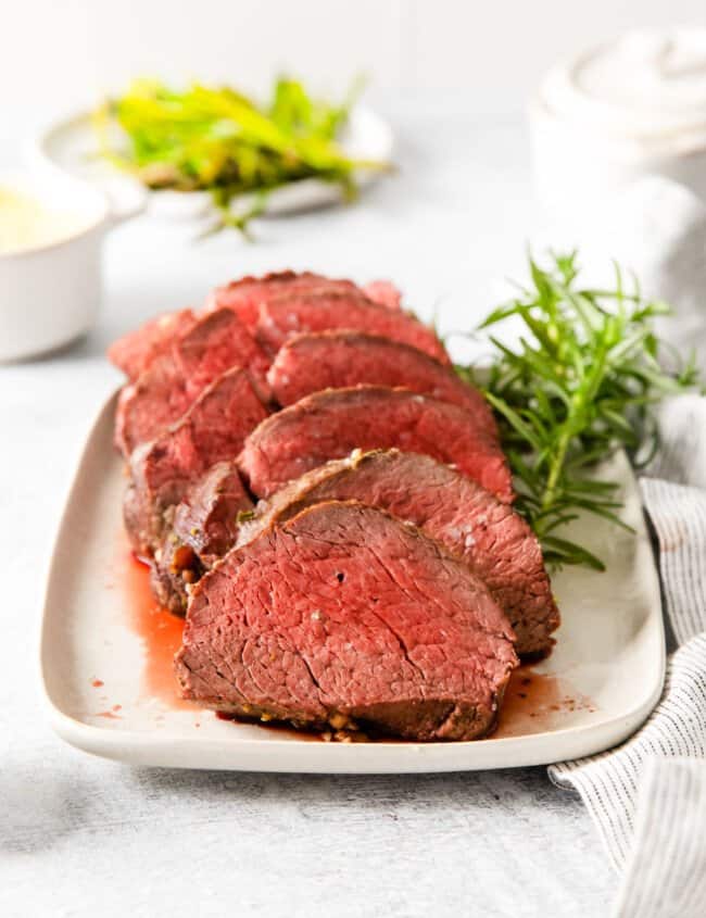 sliced crockpot beef tenderloin on a white plate.