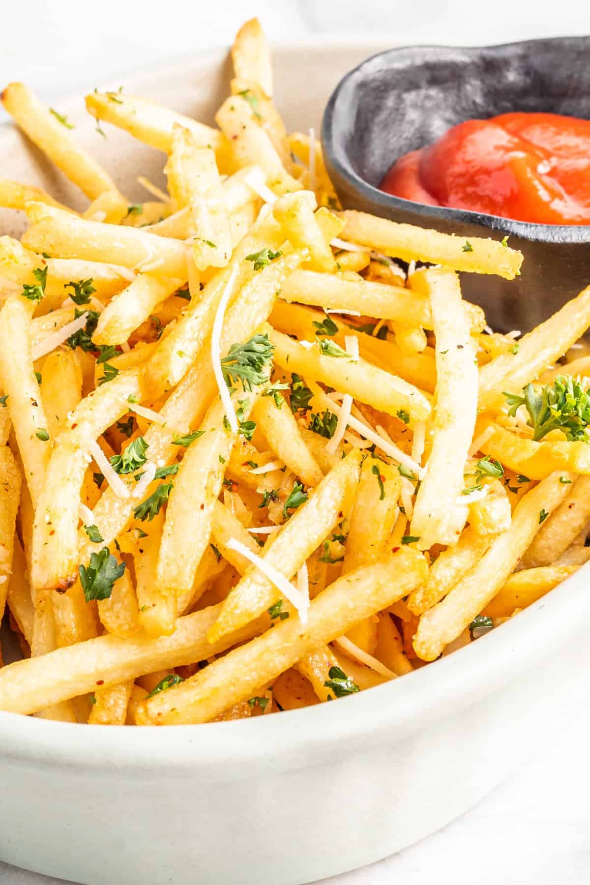 garlic parmesan fries in a white bowl with ketchup.