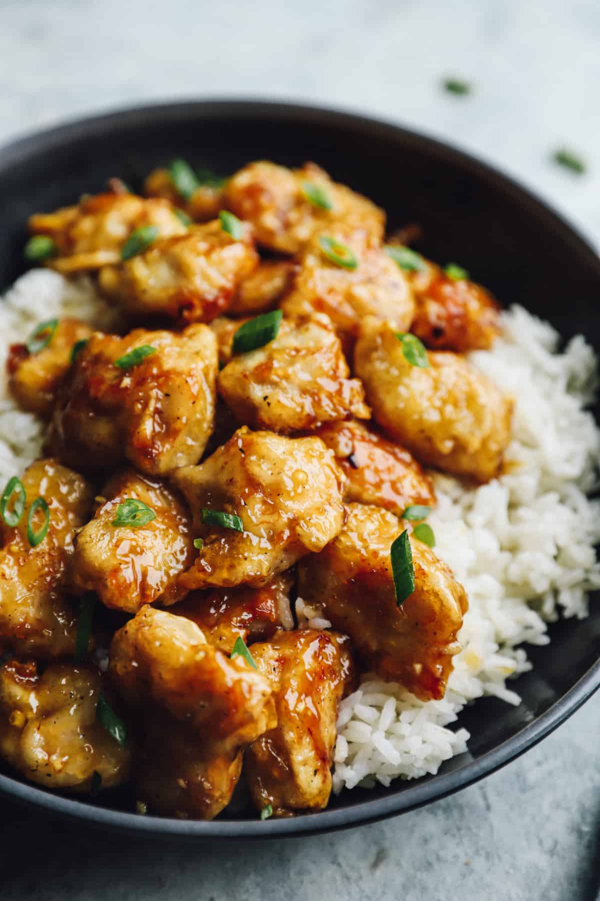 honey chicken over white rice in a black bowl.