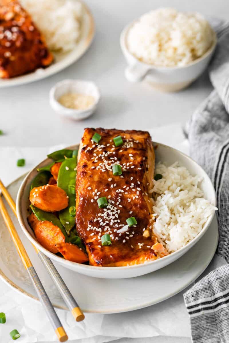 air fryer miso salmon in a white bowl with rice carrots and snap peas.