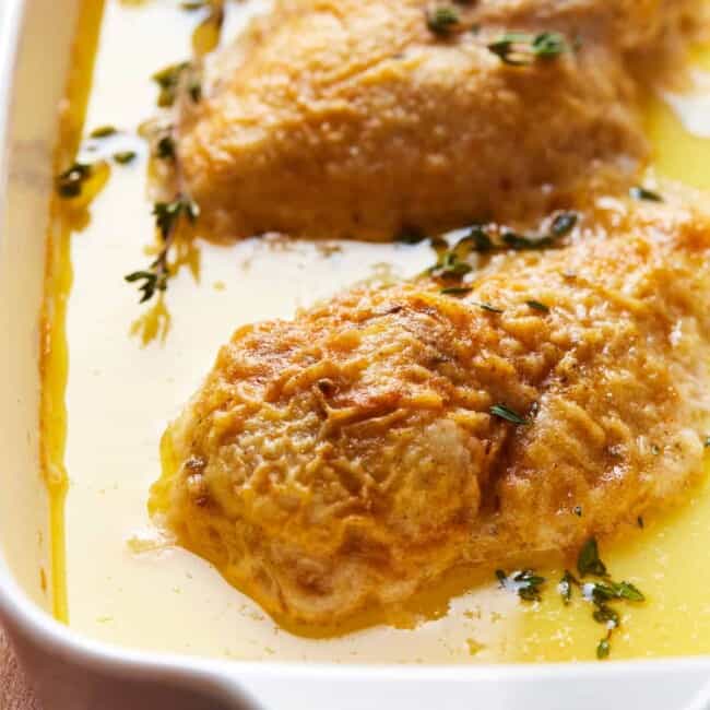 chicken in a baking dish surrounded by butter and cream