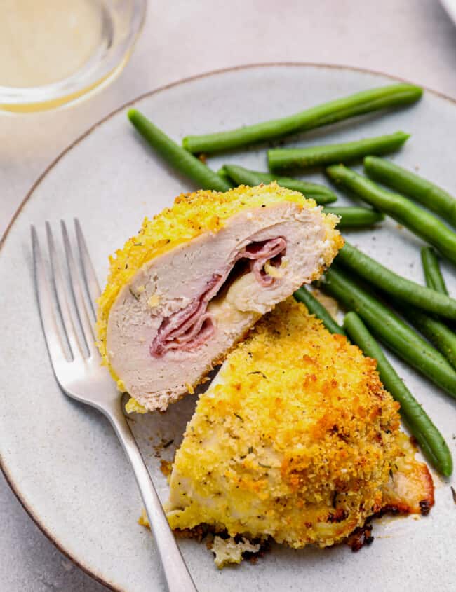 sliced chicken cordon bleu baked on a white plate with green beans and a fork.