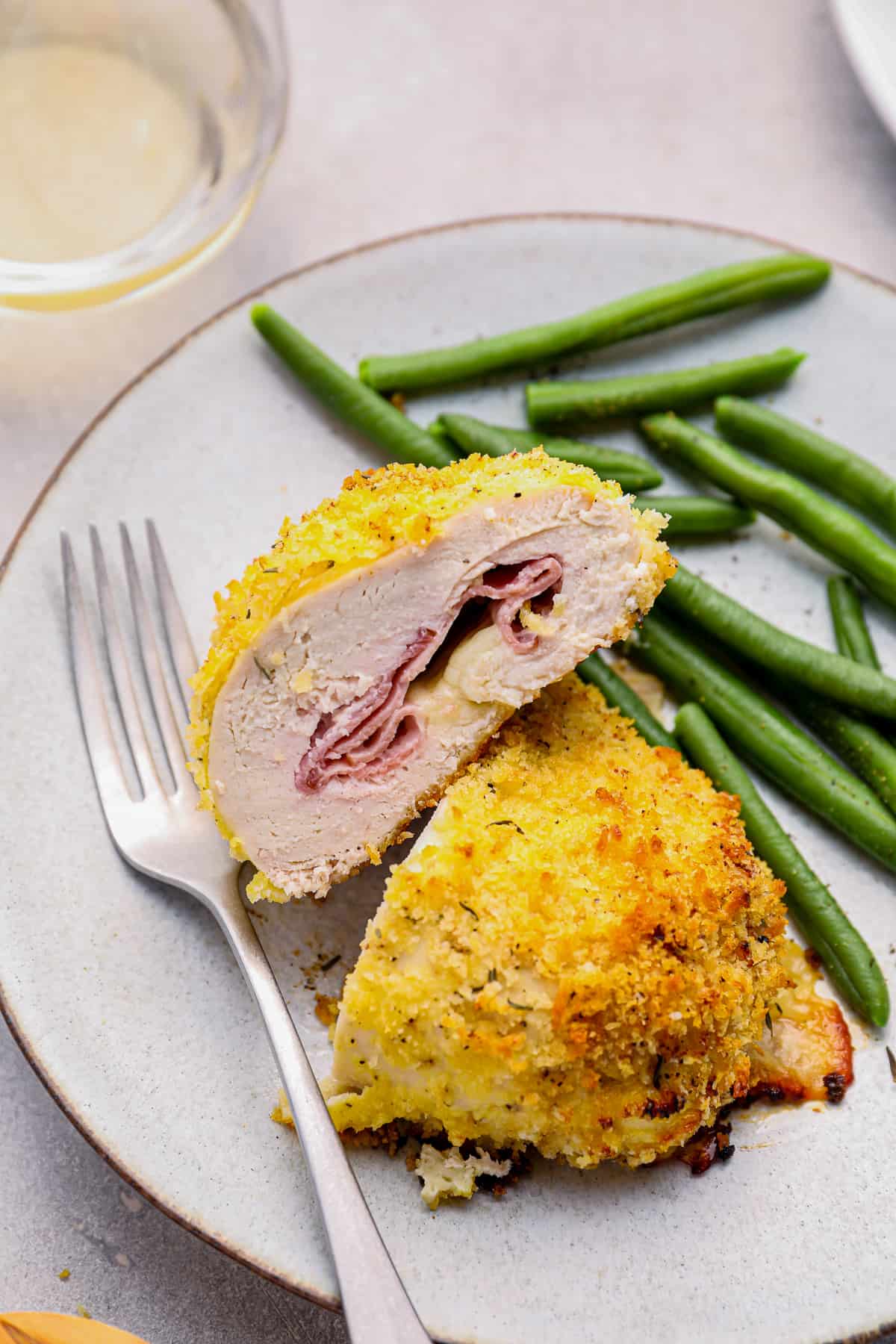 sliced chicken cordon bleu baked on a white plate with green beans and a fork.