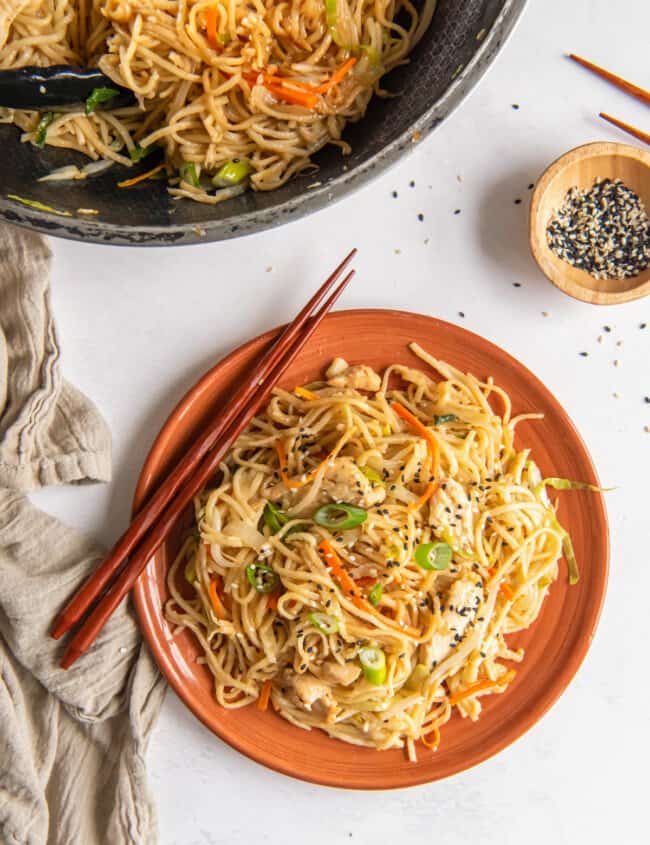 chicken lo mein on an orange plate with chopsticks.