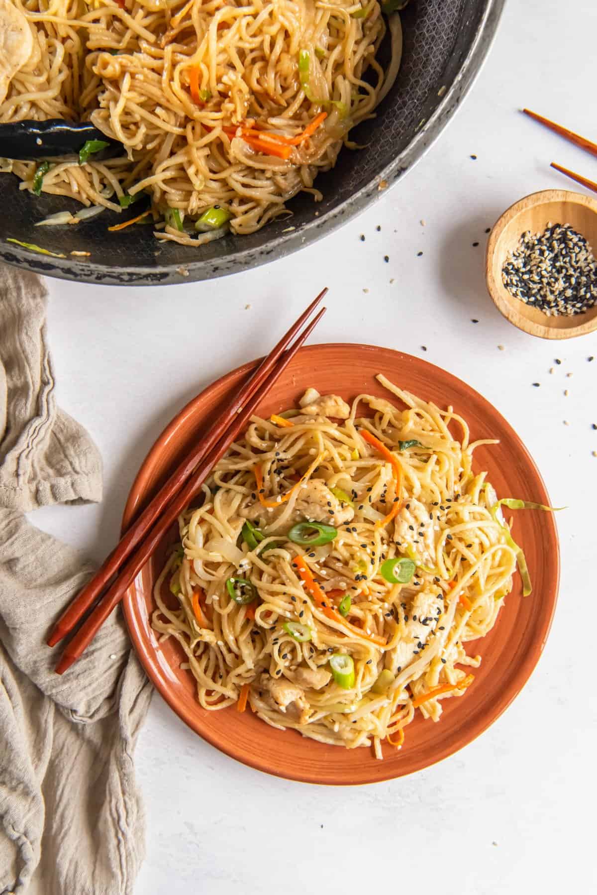 chicken lo mein on an orange plate with chopsticks.