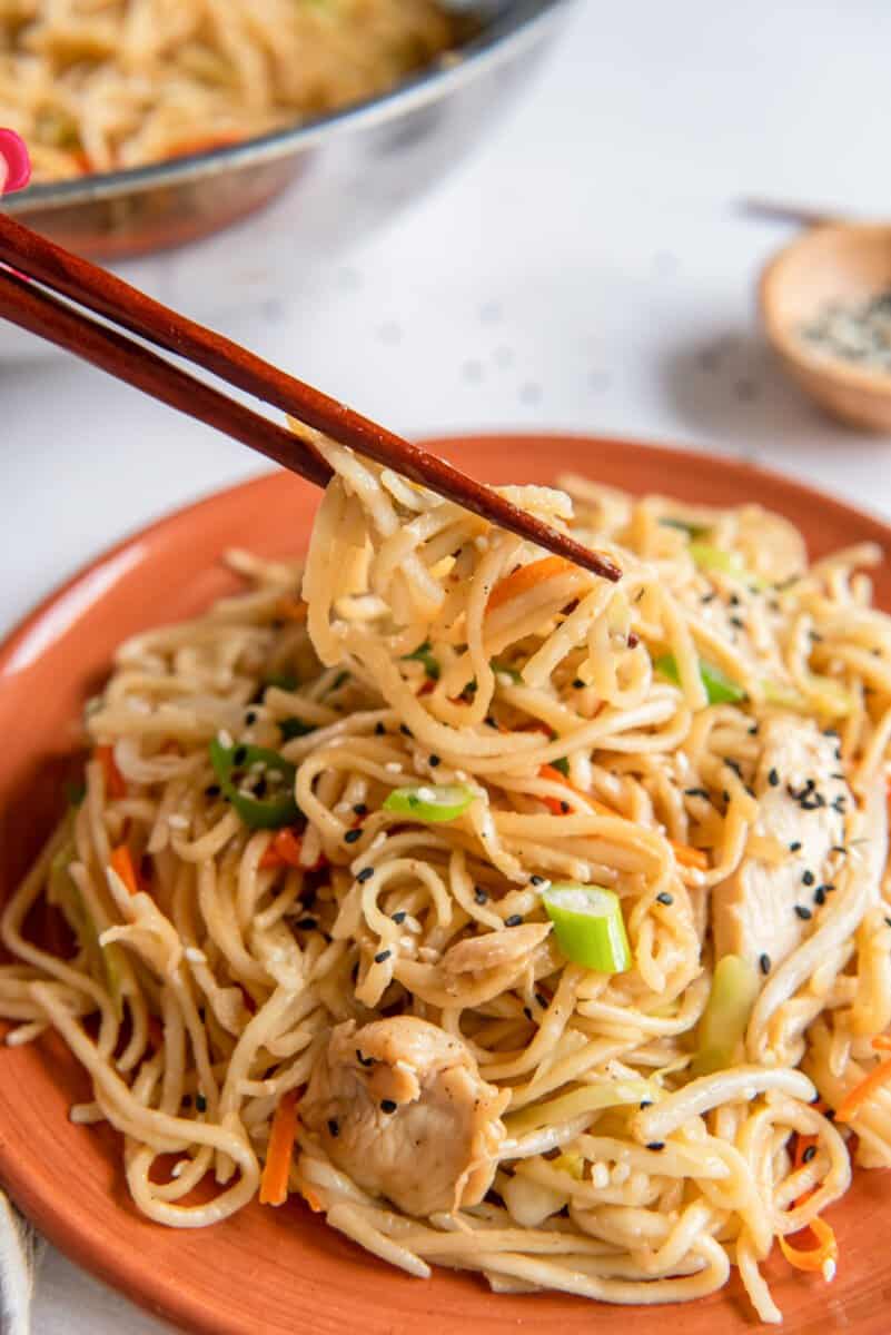 chopsticks grabbing noodles from a plate of chicken lo mein.