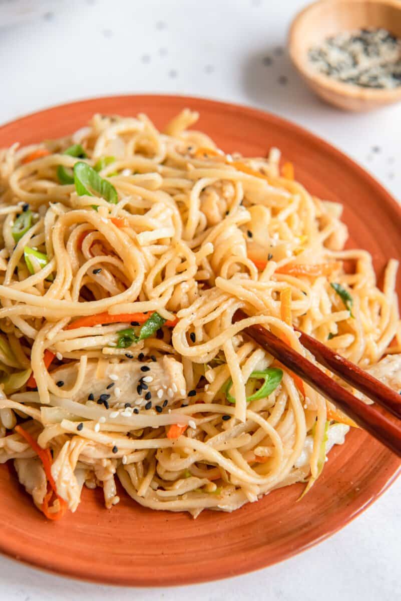 chopsticks grabbing noodles from a plate of chicken lo mein.