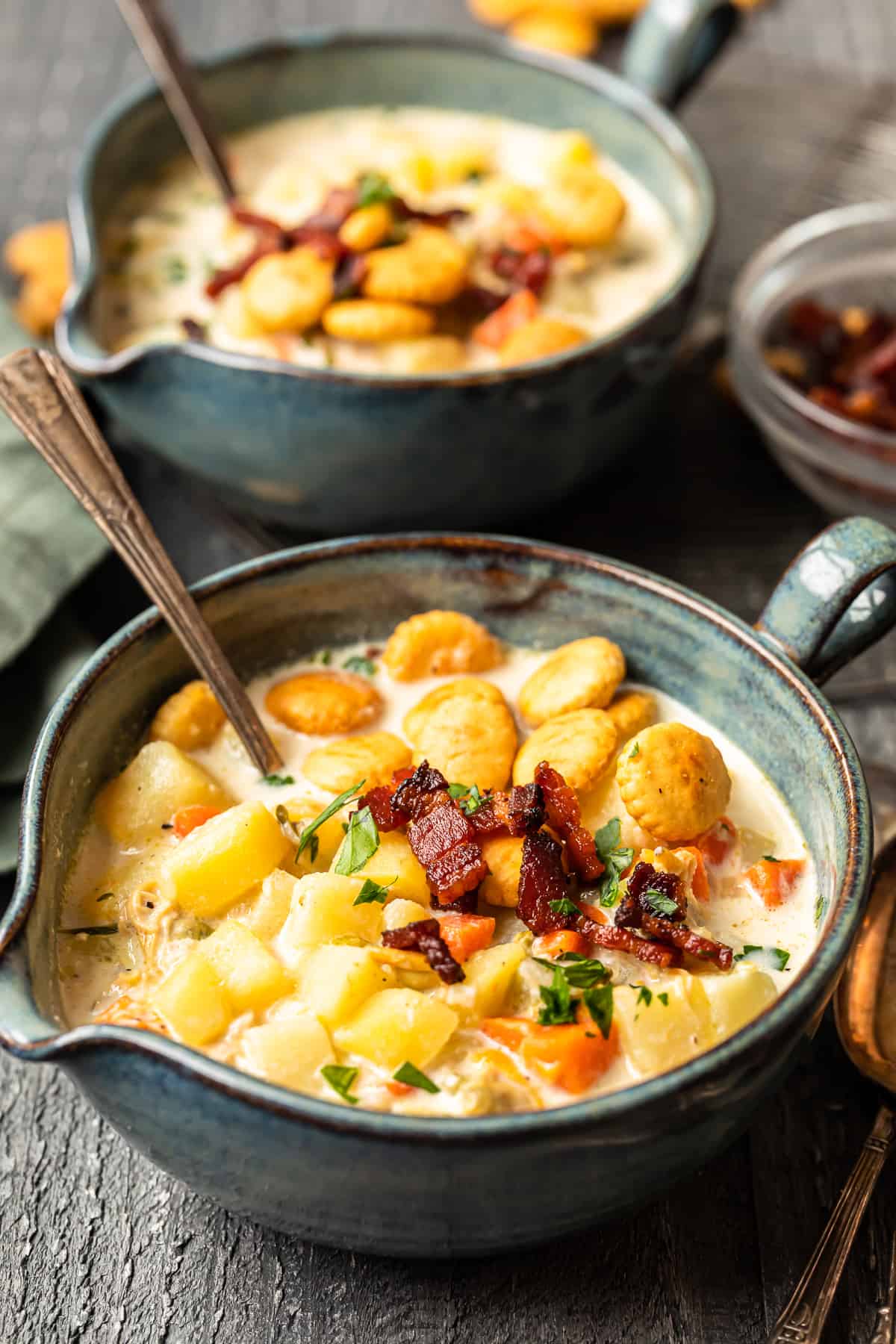 new england clam chowder in gray bowls with oyster crackers and spoons.