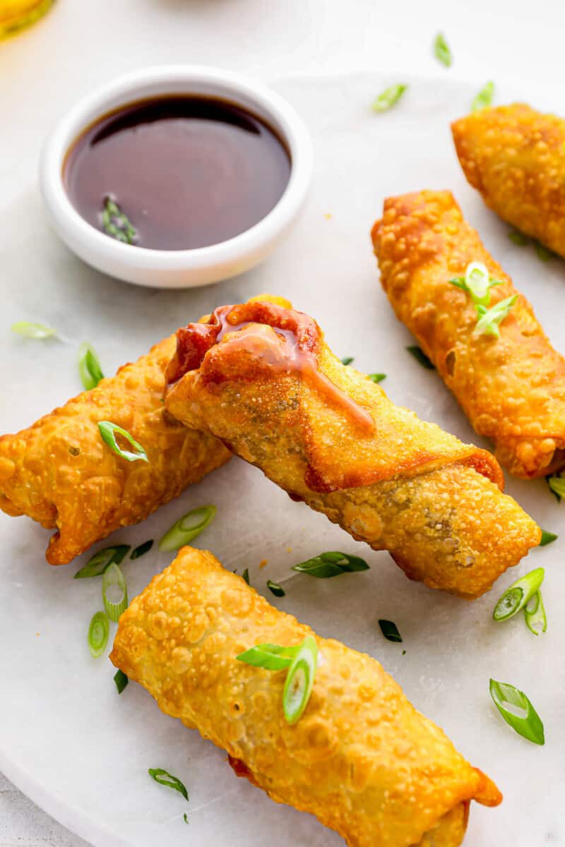 5 egg rolls on a white plate with dipping sauce.