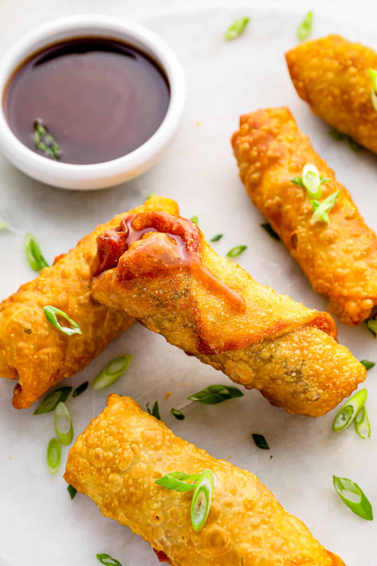 5 egg rolls on a white plate with dipping sauce.