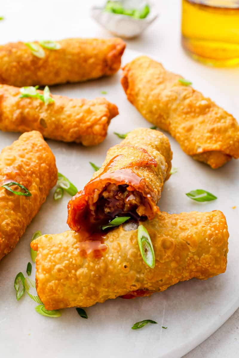 close up of bitten egg roll on a white plate with 5 egg rolls.