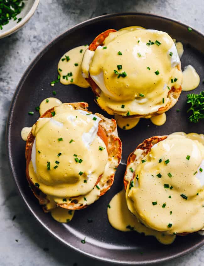 3 eggs benedict on a black plate.