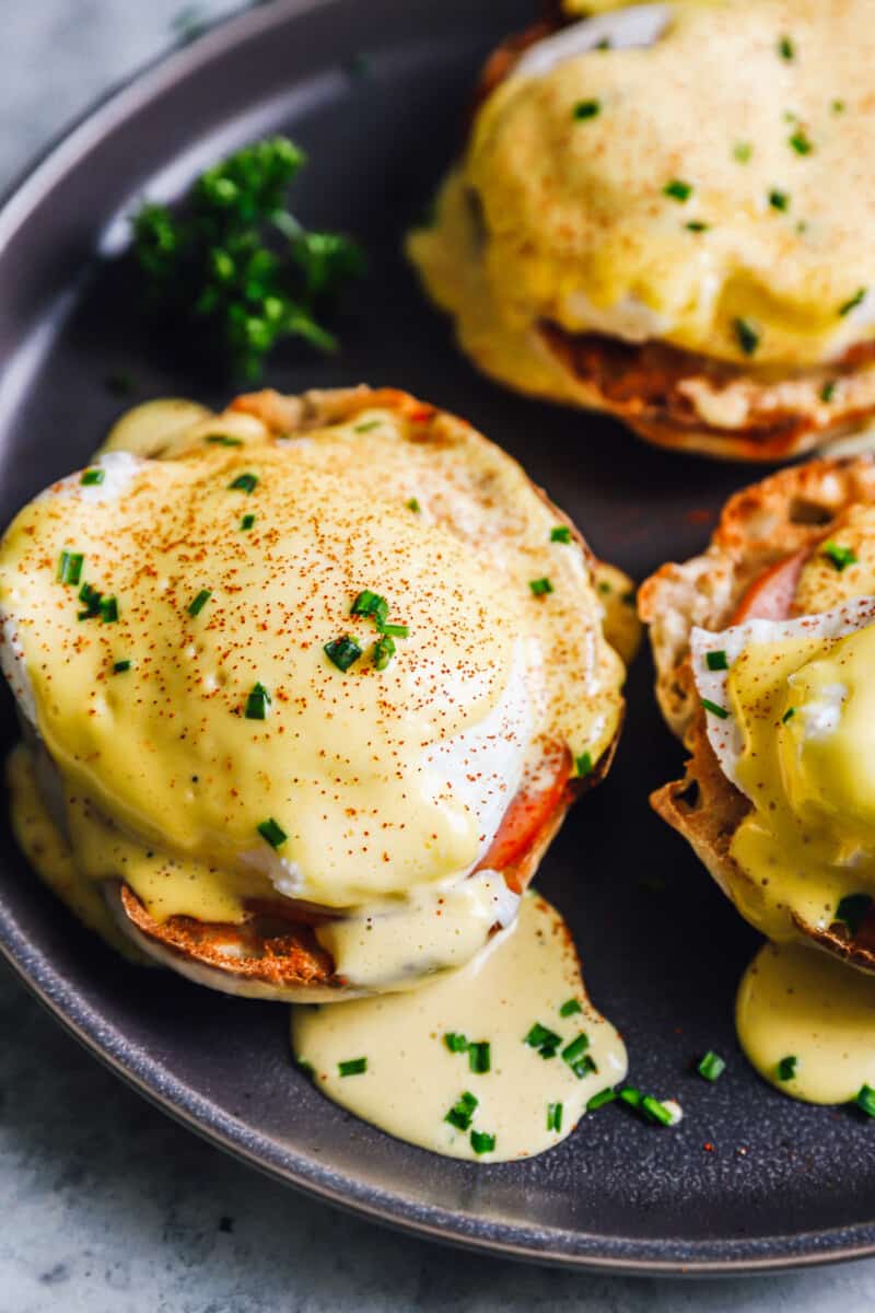 close up of eggs benedict on a black plate.