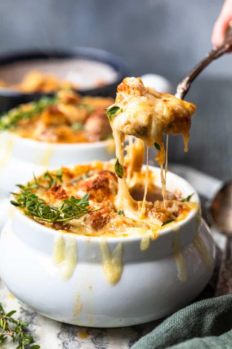 a spoonful of french onion soup hovering over french onion soup in a white bowl.