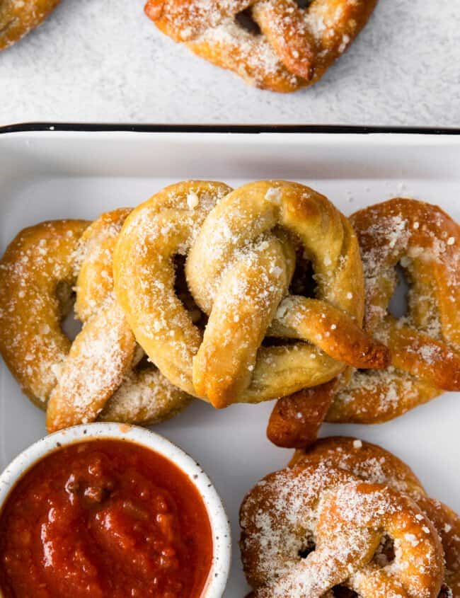 close up of garlic parmesan soft pretzels in a white serving tray with marinara sauce.